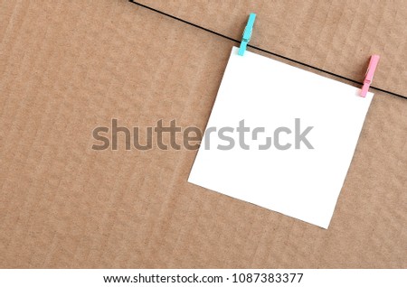 White blank card on rope on a brown cardboard background. Creative reminder, small sheet of paper on wooden clothespin, memo backdrop