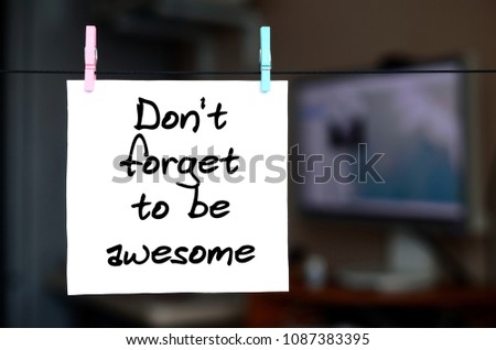 Don't forget to be awesome. Note is written on a white sticker that hangs with a clothespin on a rope on a background of office interior