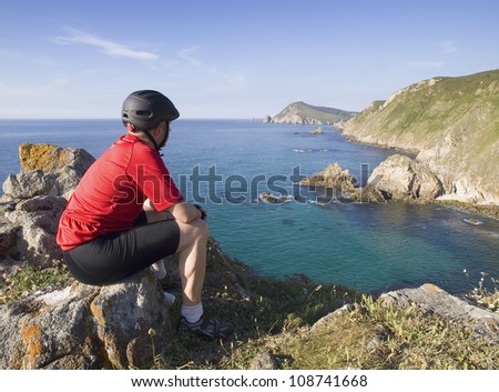 Cyclist sitting, staring at a coastal landscape on a sunny day and after sports. the picture was taken in Ferrol, Galicia, Spain.