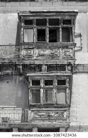 Building with traditional maltese balcony in historical part of Valletta. Damaged windows on the facade of a abandoned house in Malta. Black and white picture