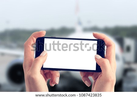 Woman waiting to fly and uses the smartphone. Two hands are holding a smartphone with a blank screen and a copy space. Blurred background.