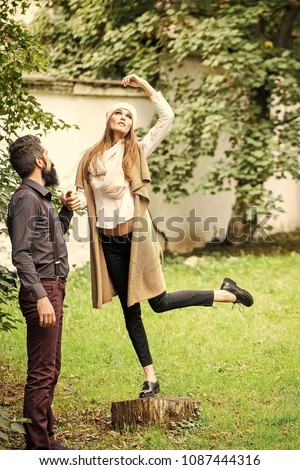 Beautiful young fashionable emotional expressive couple of slim woman and man with long lush black beard standing together on fresh green grass outdoor on autumn natural background, vertical picture