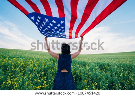 Woman holding the american flag outdoors on a meadow.  4th of July - Independence day. 