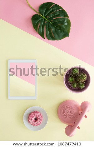 Top view of a duotone table with a green leaf, cactus, tablet, doughnut and retro phone