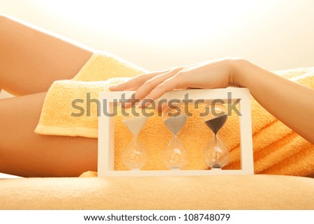 closeup picture of female hands and legs in spa salon with a sandglass