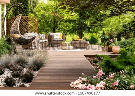 Beautiful wooden terrace with garden furniture surrounded by greenery on a warm, summer day Royalty-Free Stock Photo #1087490177