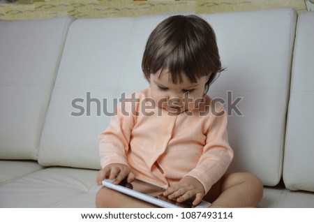 Toddler girl playing with digital tablet on couch at home. baby girl uses a tablet as a phone, plays, calls, laughs
