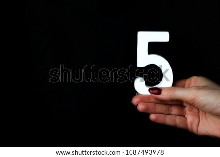 On a black background, female hand with number five.