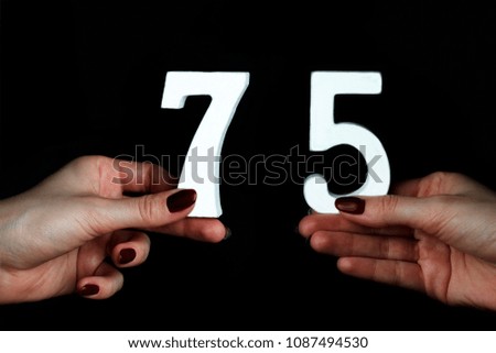 On a black background, female hand with numbers seventy-five.