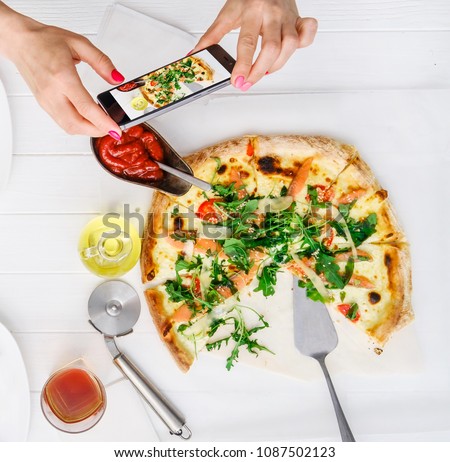Girl takes pictures of seafood pizza and sauces on white wood table