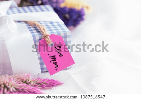 Happy mother's day concept. Pink Gift box with purple flower, paper tag with LOVE MOM text and two handmade red heart on white cheesecloth background.