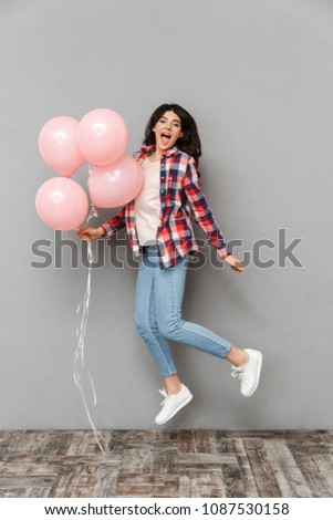 Image of cute beautiful young lady jumping isolated over grey background wall holding balloons.