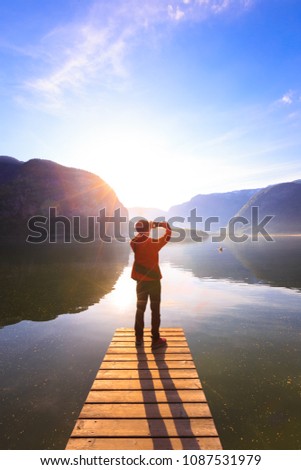 Back view of young man takes pictures by cellphone with a beautiful landscape and sun flare as lens glare