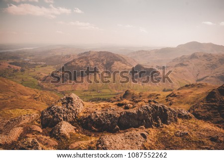 View over the Langdale Valley from a mountain in The Lake District, Cumbria UK. Warm summer day with rocky foreground and hazy sky in the background.