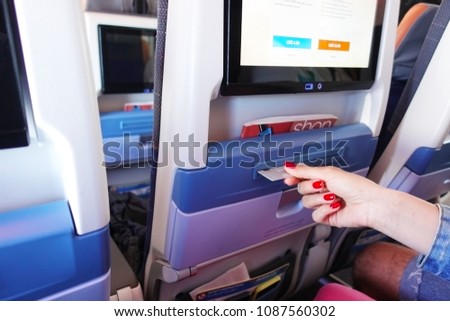 Woman paying by credit card through a modern terminal located behind the front seat, inside the airplane, during the flight
