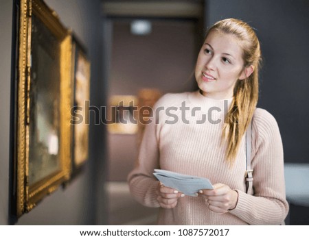 Portrait of young woman with guide looking at pictures in museum of the arts 