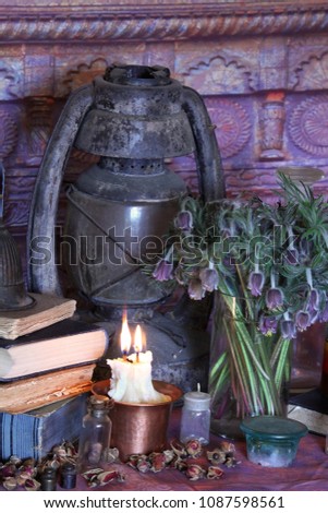Still Live: Old oil lamps, antique books, dried rose buds, a burning candle in a copper bowl, medicine bottles, lavender, Pulsatilla pratensis on an antique background. Wicca background.