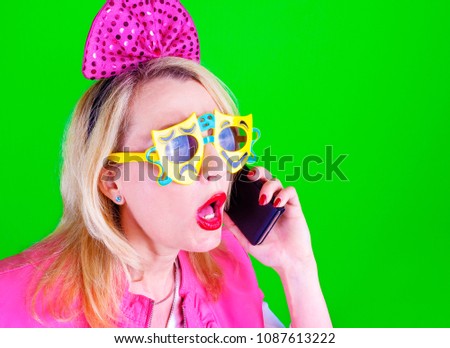 Crazy comedian blonde female in a pink suit in a funny carnival glasses is calling by phone on a colored background