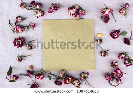 Romantic composition with purple dry rose buds and paper blank on textile linen background. Concept for greeting card for valentine or birthday. Love theme. Shabby chic