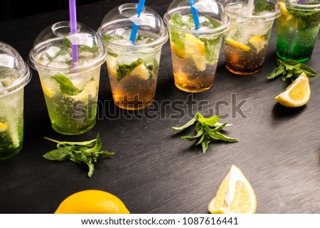 fresh mojito cocktail with lime, mint and blue drinking straw in plastic cup on black background