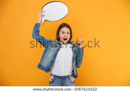 Portrait of an excited little schoolgirl holding empty speech bubble over yellow background