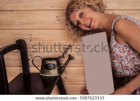 A young smiling woman assists in making photo of a vintage watering can with a barberry branch. She keeps a white cardboard in her hands to give more light to a photo. Concept - emotion of joy.