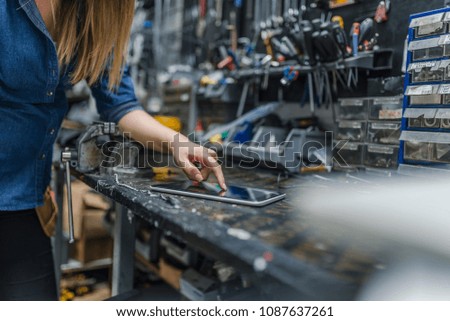 Female mechanic at work. Using a tablet while fixing a bicycle. Female bicycle repair technician using digital tablet in bicycle shop. Mechanic woman checking something on a tablet-pc and checklist.
