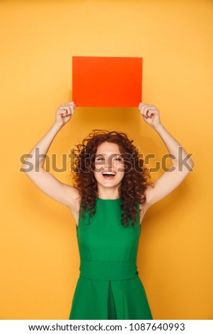 Portrait of a joyful redhead woman in dress holding empty copy space isolated over yellow background