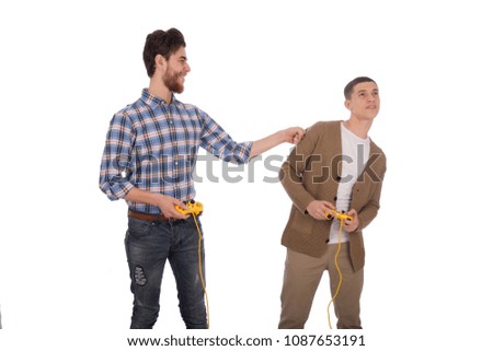 Two friends playing together holding the joystick in hands one hitting his friends with his fist in shoulder joking, isolated on a white background.