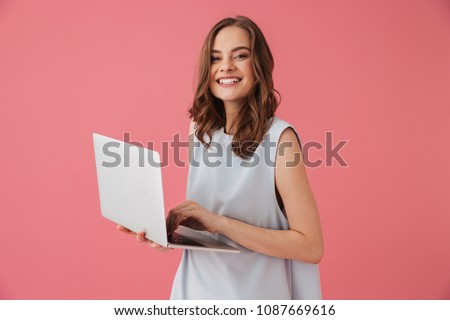 Image of cheerful young woman standing isolated over pink background using laptop computer. Looking camera. Royalty-Free Stock Photo #1087669616