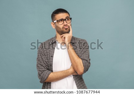 Portrait of bearded thoughtful handsome man with black glasses in casual style thinking. studio shot on blue background. Royalty-Free Stock Photo #1087677944