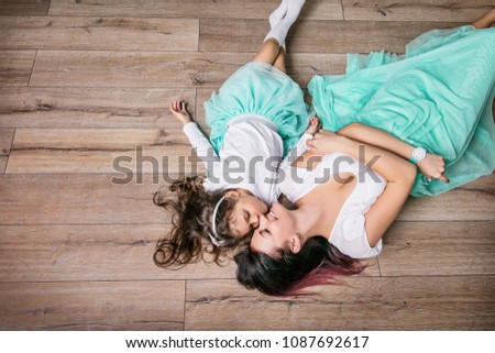 Mother and daughter beautiful and happy in turquoise skirts lie on laminate flooring home top view