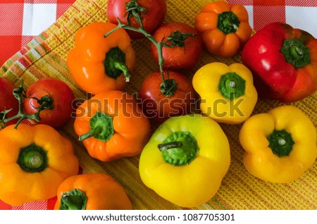 Fresh paprika and branch of tomatoes, on yellow towel and red checkered background, organic summer vegetables