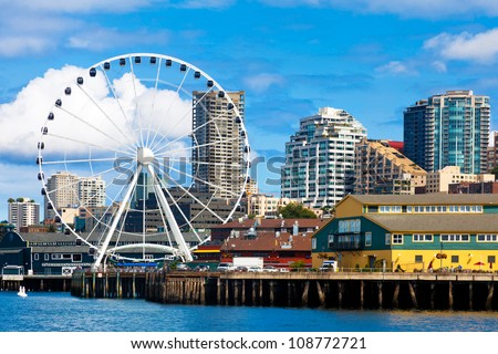 Seattle ferris wheel, waterfront and skyline on a bright sunny day with blue sky and clouds.  View is from the water.  Close up