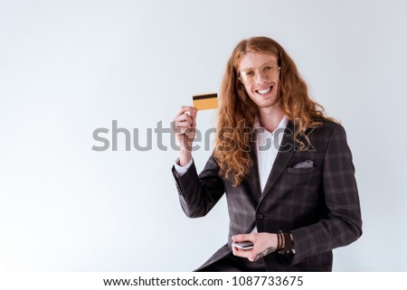 smiling tattooed businessman with curly hair showing credit card isolated on white