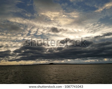 Dark floating gray storm clouds over the water with sunset sky