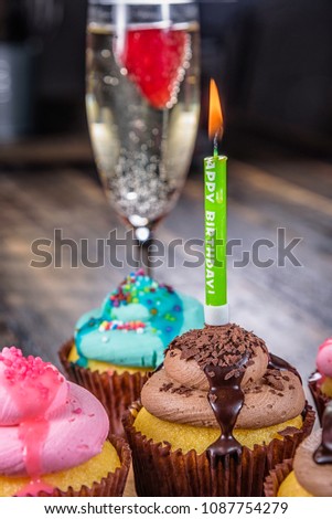 Several cupcakes on a wooden cutting board with a Happy Birthday candle and glass of Champagne