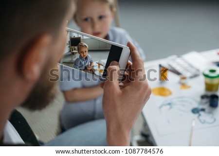 partial view of man taking photo of sons picture on smartphone at home