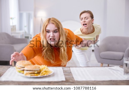 Stop. Excited stout woman reaching for a sandwich and her friend holding her Royalty-Free Stock Photo #1087788116
