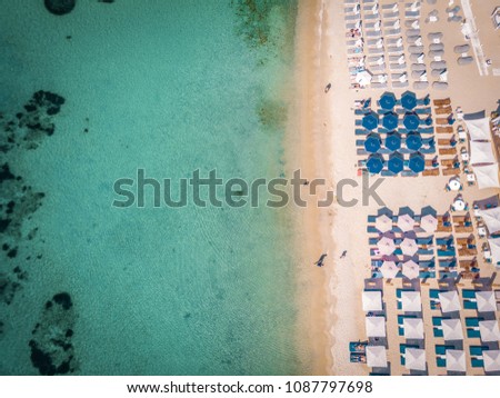 beach from the sky with colorful umbrellas and beach bed chair, blue ocean drone shot, Mykonos Island Greece 