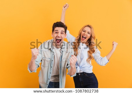 Portrait of cheerful people man and woman in basic clothing smiling and clenching fists like winners or happy people isolated over yellow background Royalty-Free Stock Photo #1087802738