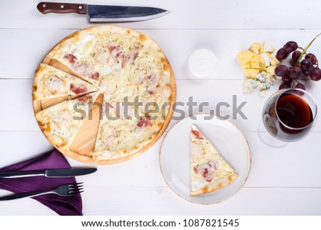 Fresh cheese pizza with ham and cream sauce on wooden board, glass of red wine, grapes, cheese and cutlery on napkin, copy space. Italian traditional cuisine. Top view, flat lay