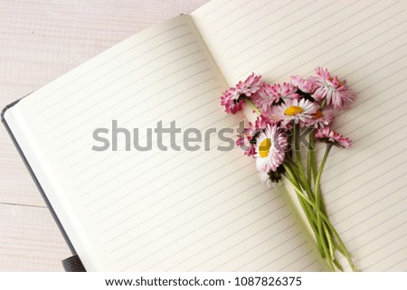 Fine romantic composition with open paper notebook with lines on pages and beautiful bunch of pink daisy. Dreaming concept. Day planing theme. Simple composition on white wooden background