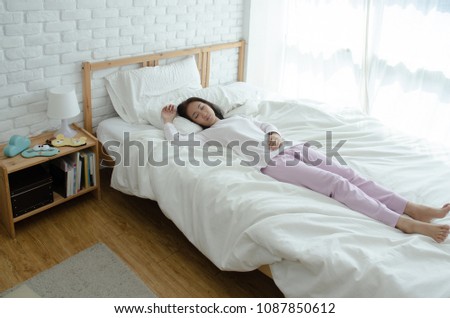 Beautiful womem sleeping in the bedroom. Sleeping in a white room makes you feel comfortable.Asian girl wearing pink pants, white coat curled In bed in a white room .Do not focus on objects.