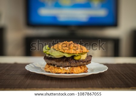 LCHF Low carbohydrate high fat burger or hamburger meal. LCHF burger with non carbohydrate bread made of sesame, eggs, chees, almonds. Concept picture of a LCHF burger in front of television screen.