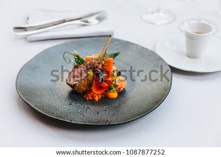 Modern French cuisine: Roasted Lamb neck & rack served with carrot, yellow curry served in black stone plate with fork and knife. Royalty-Free Stock Photo #1087877252