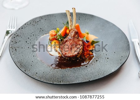 Modern French cuisine: Roasted Lamb neck & rack served with carrot, yellow curry and lamb sauce. Served in black stone plate with fork and knife. Royalty-Free Stock Photo #1087877255