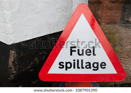 Red and white triangular road safety fuel spillage sign warning black text on white background against wall with copy space