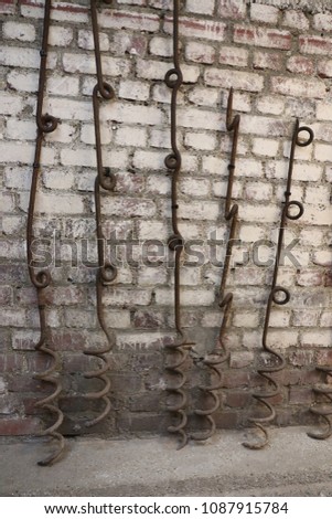 View of a group of metallic wire pickets looking like corkscrews. Ancient objects used to support the barbed wire entanglements during the world war 1. White painted bricks wall in background.