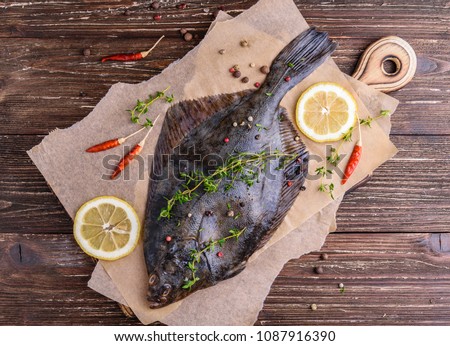 Raw flounder plaice fish (flatfish). Cooking process concept. Flounder fish with spices, lemon slices, thyme on parchment paper. Dark wooden table background. Top view.